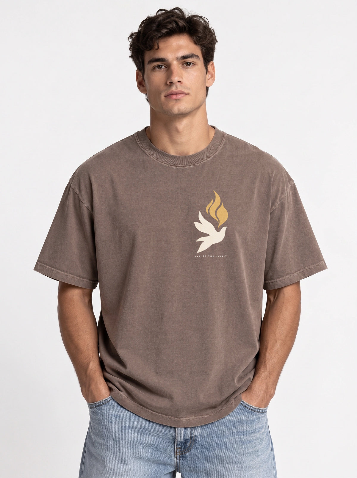 Person wearing a faded brown T-shirt with a small white dove, gold flames, and “LED BY THE SPIRIT” on the chest.
