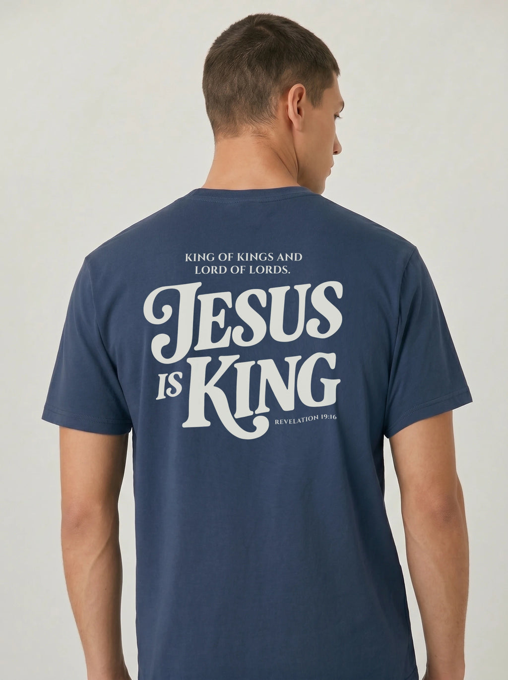 Person wearing a navy T-shirt with cream back text: “King of Kings and Lord of Lords. Jesus is King. Revelation 19:16.”