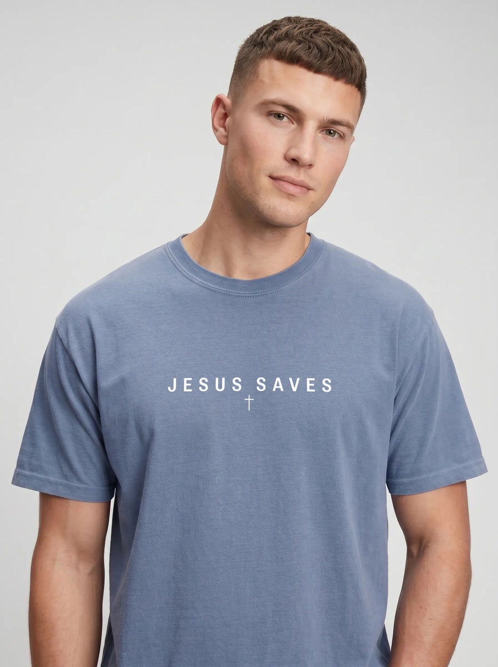A man wearing a heathered blue crewneck t-shirt with a dark gray tree graphic and the text 'JESUS SAVES' printed in white across the chest, set against a plain light gray background.