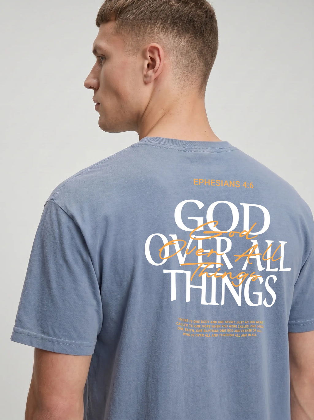 Person wearing a washed blue T-shirt with a small chest graphic reading “God Over All Things.”