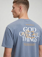 Person wearing a washed blue T-shirt with a small chest graphic reading “God Over All Things.”