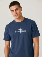 A man wearing a navy blue crewneck t-shirt with a white graphic on the chest that reads 'jesus saves' beneath a cross, set against a plain light gray background.