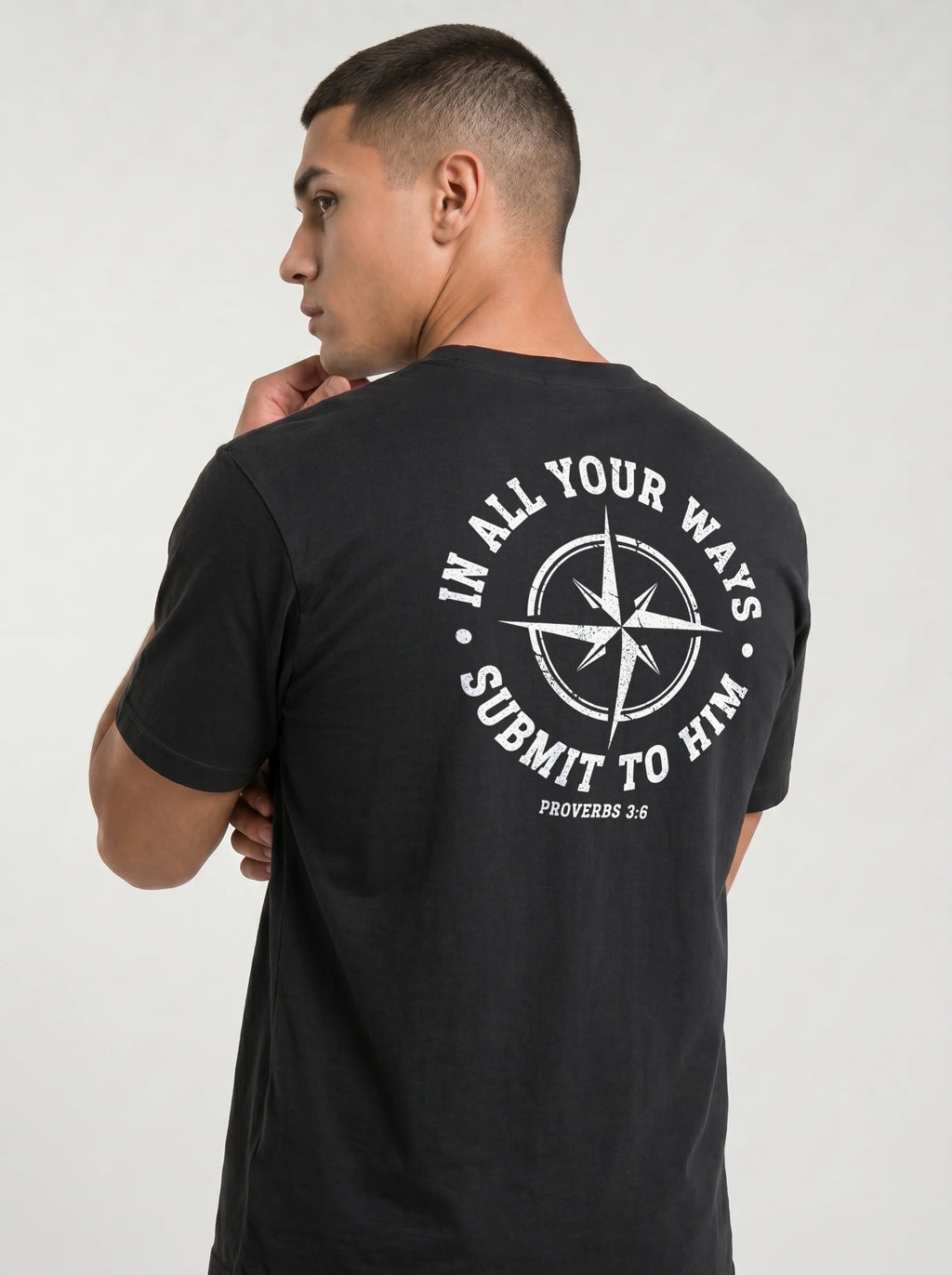 A man wearing a black t-shirt, viewed from the back. The shirt features a large white graphic print on the back with a compass rose and the text 'IN ALL YOUR WAYS SUBMIT TO HIM PROVERBS 3:6'.