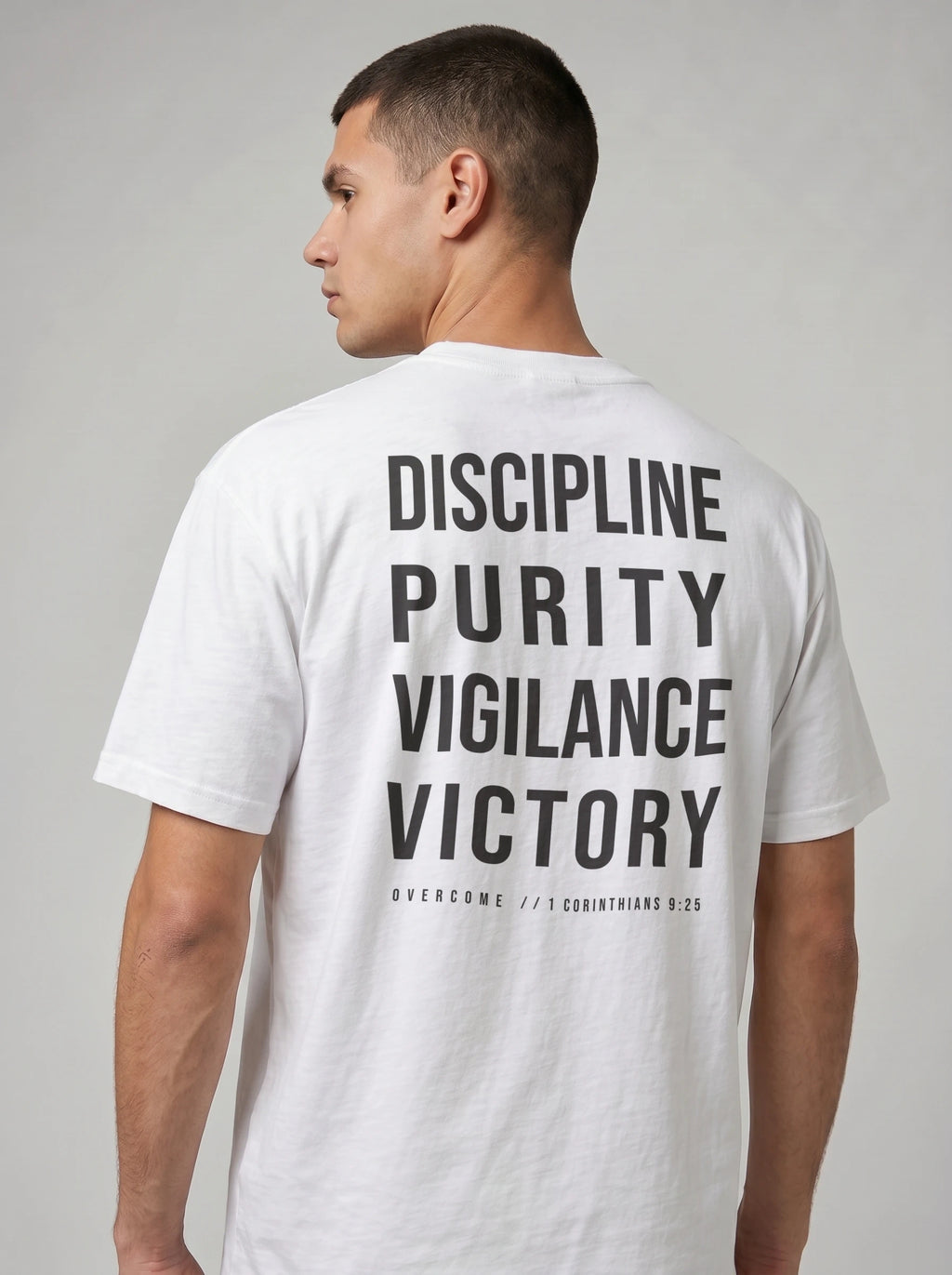 Person wearing a white T-shirt with large back text reading “Discipline Purity Vigilance Victory” and “Overcome // 1 Corinthians 9:25.”