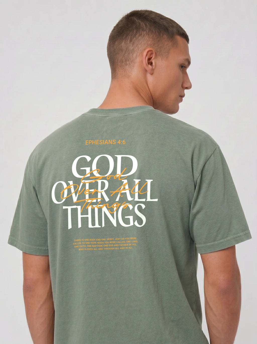 Person wearing a sage green T-shirt with “Ephesians 4:6,” a large “God Over All Things” back graphic, and Bible verse text.