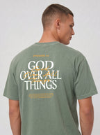 Person wearing a sage green T-shirt with “Ephesians 4:6,” a large “God Over All Things” back graphic, and Bible verse text.