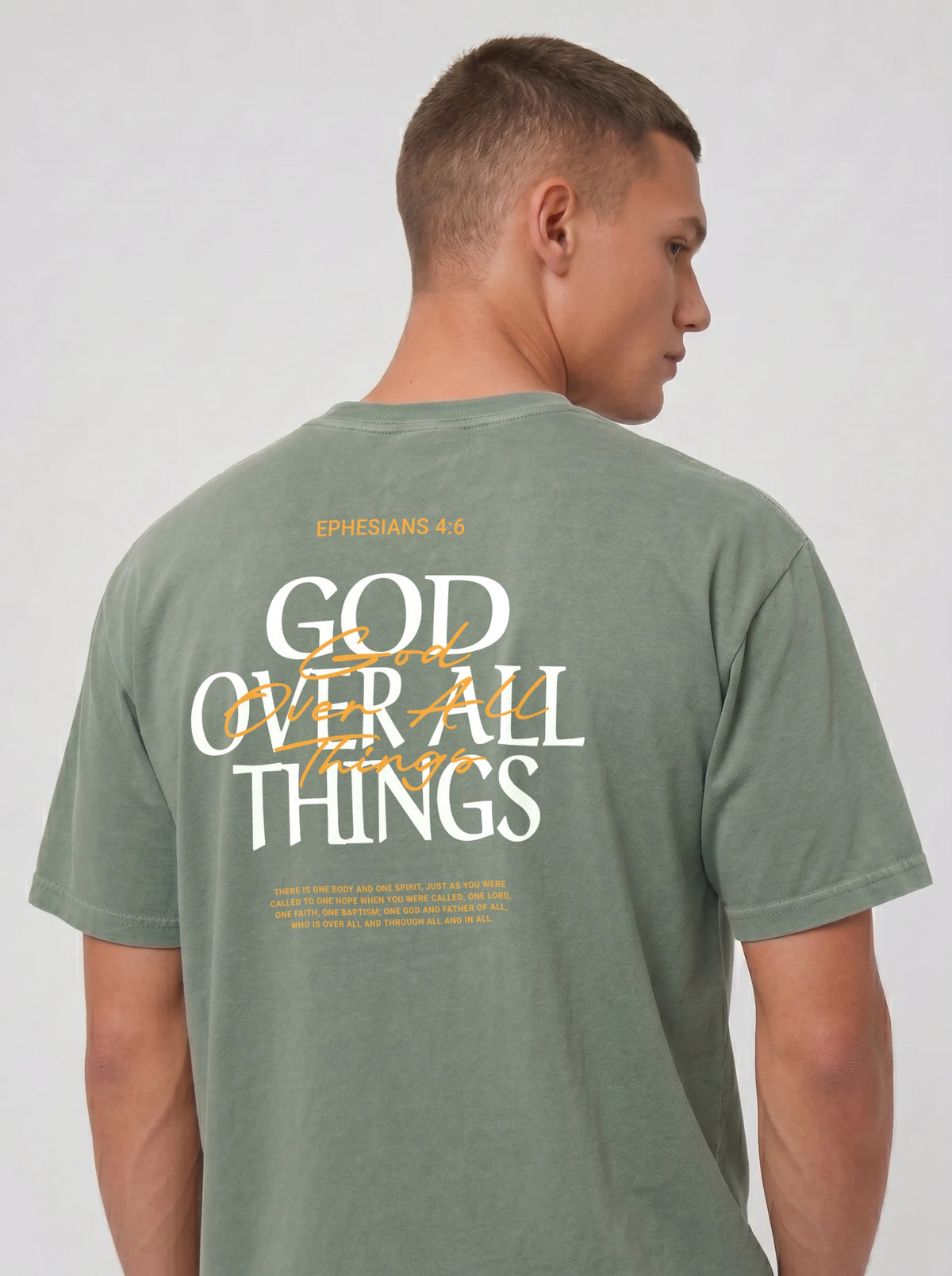 Person wearing a sage green T-shirt with “Ephesians 4:6,” a large “God Over All Things” back graphic, and Bible verse text.