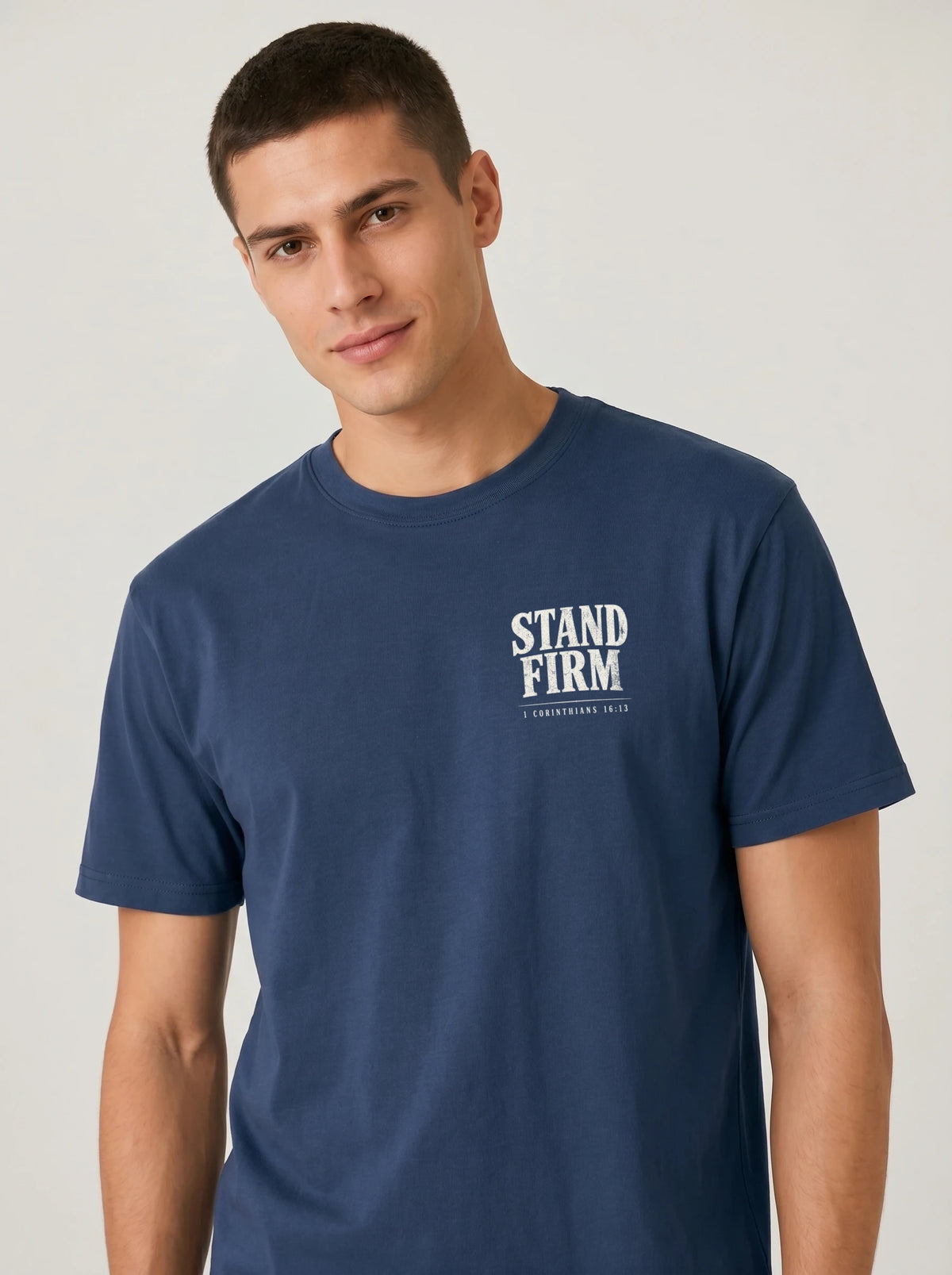 A man wearing a navy blue crewneck t-shirt with a white graphic print on the left chest that reads 'STAND FIRM'.