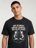 A man wearing a black graphic t-shirt with a white printed quote and boxing gloves design, photographed against a light gray studio background.