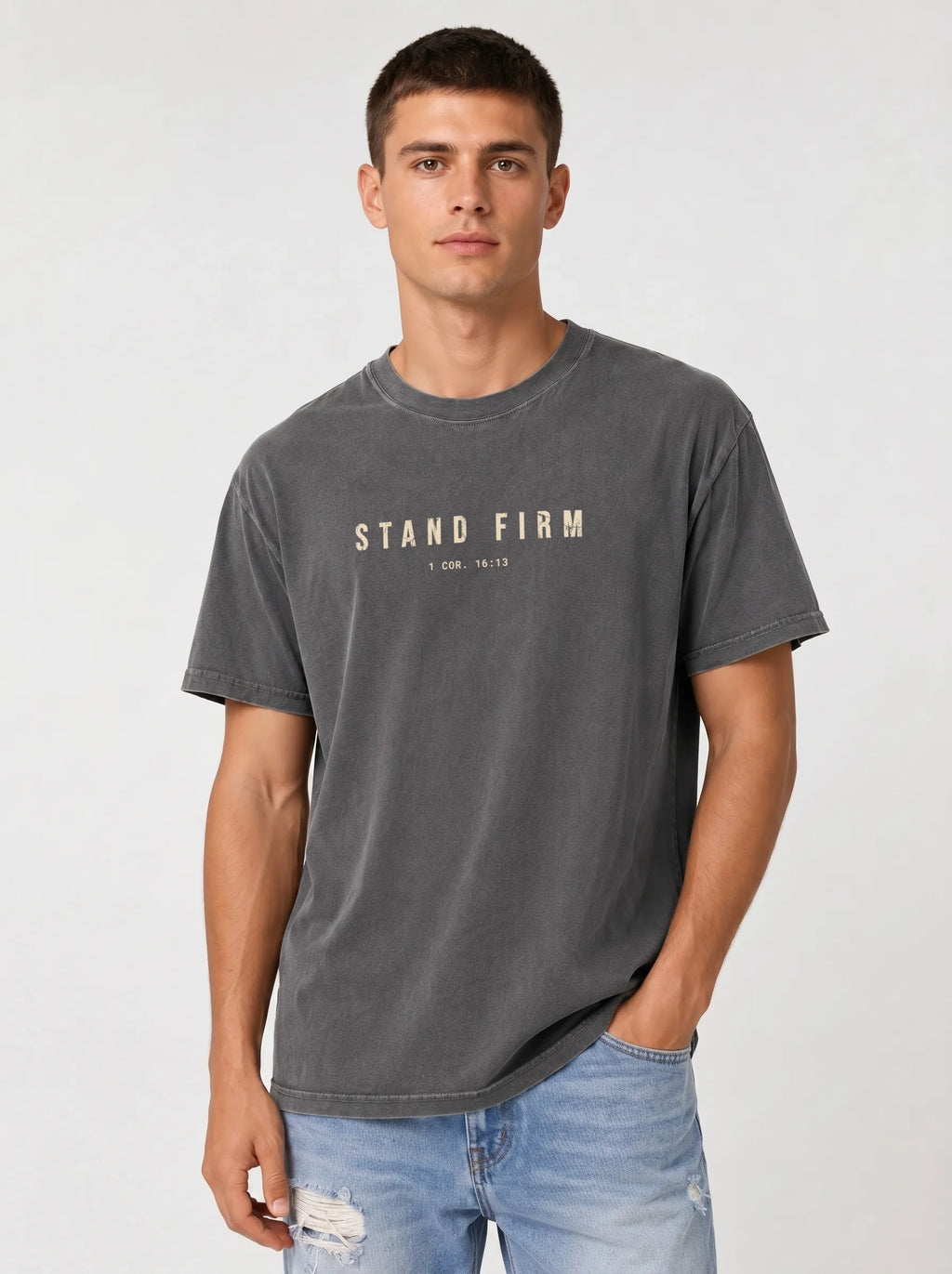 Person wearing a faded gray T-shirt with distressed beige text reading “Stand Firm” and “1 Cor. 16:13.”