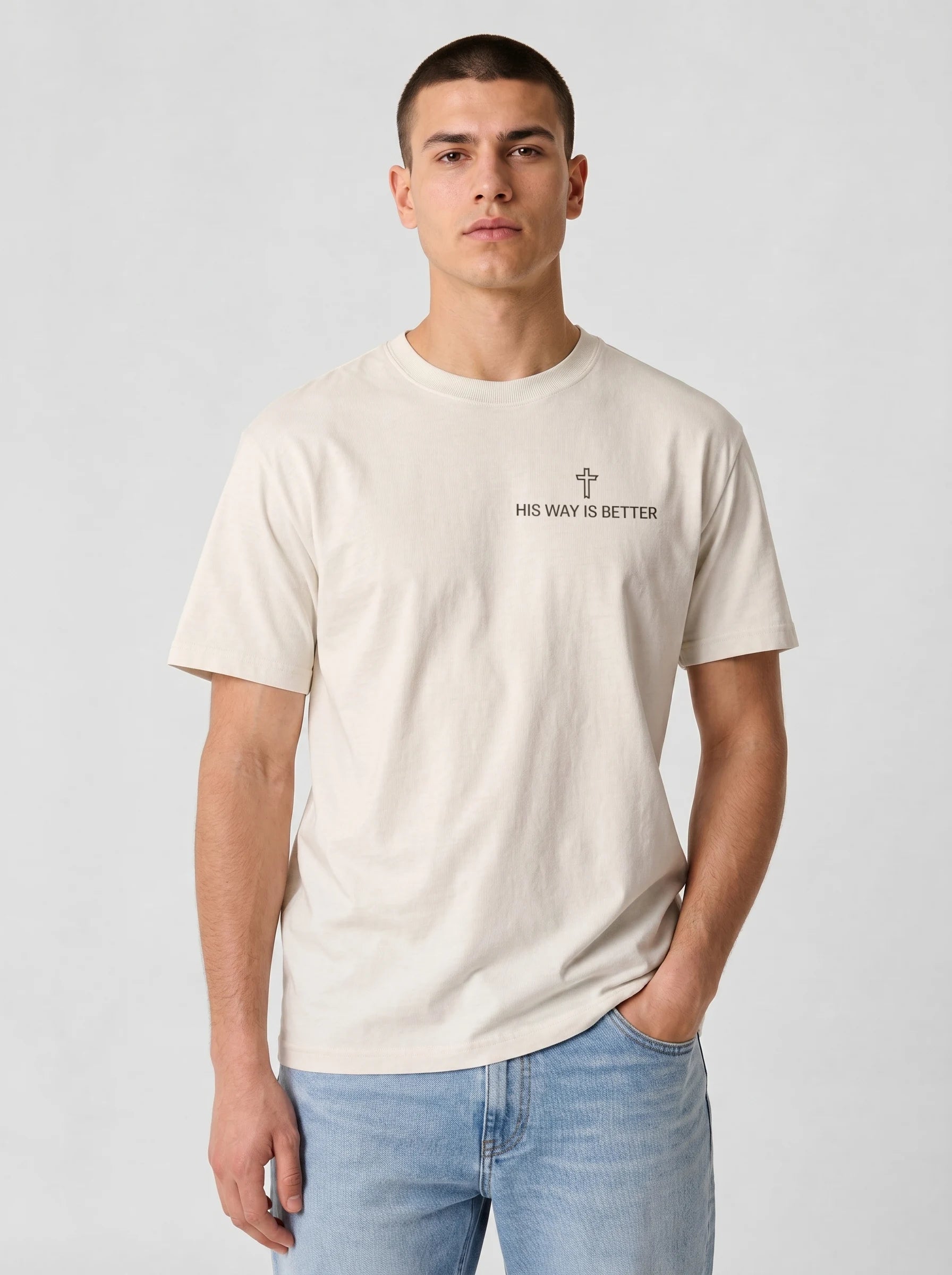 A man wearing a light beige crewneck t-shirt with a small black graphic and the text 'MY WAY IS BETTER' on the left chest, paired with light blue jeans, against a light gray studio background.
