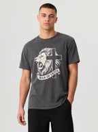 A man wearing a dark gray graphic t-shirt with a white lion and cross design that reads 'MAN OF FAITH', paired with black pants, against a light gray studio background.