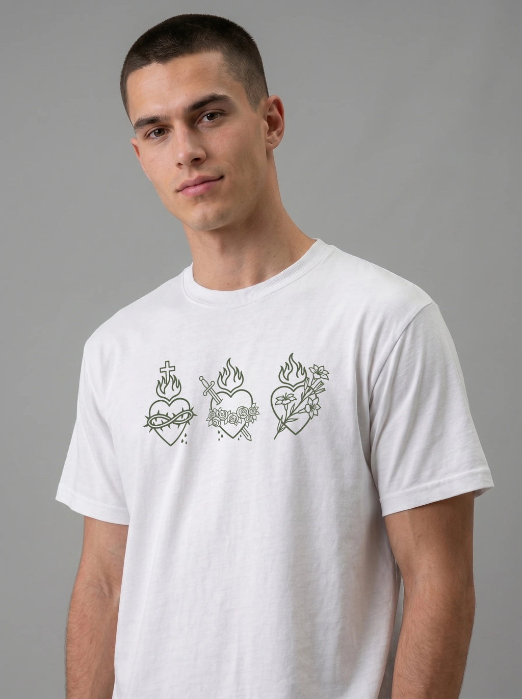 A man wearing a white crew-neck t-shirt with three green Sacred Heart of Jesus line-art graphics on the chest, set against a plain gray studio background.