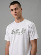 A man wearing a white crew-neck t-shirt with three green Sacred Heart of Jesus line-art graphics on the chest, set against a plain gray studio background.