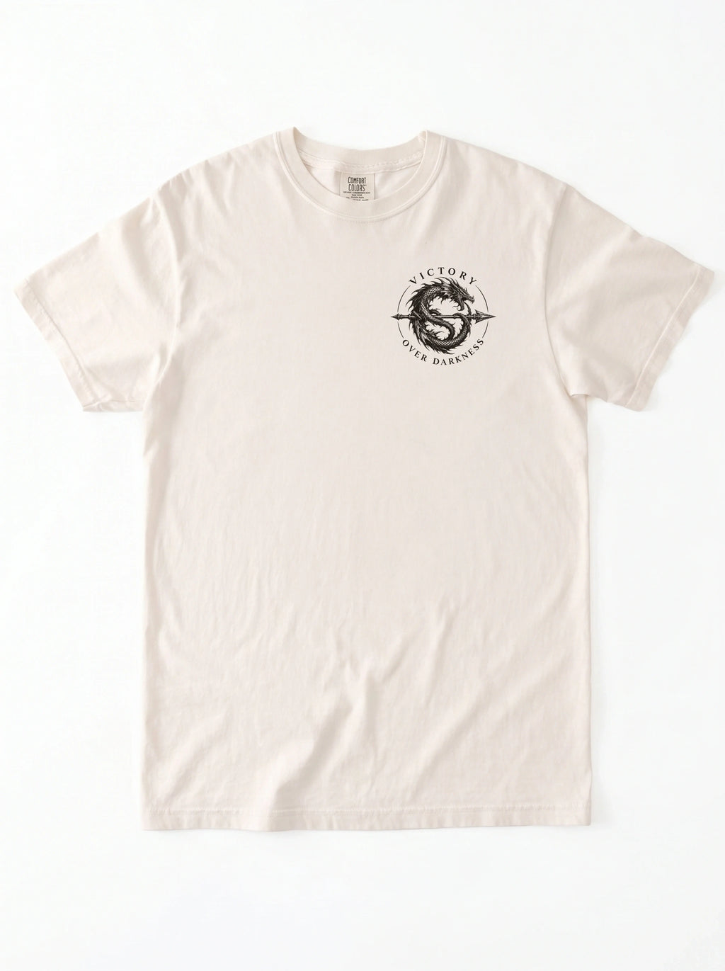 Cream T-shirt laid flat with a small circular dragon graphic and the text “VICTORY OVER DARKNESS” on the chest.