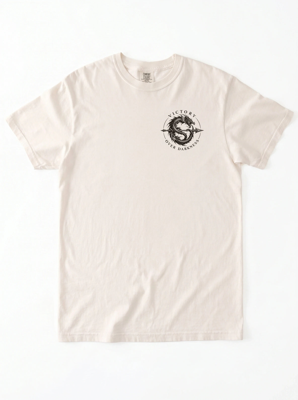 Cream T-shirt laid flat with a small circular dragon graphic and the text “VICTORY OVER DARKNESS” on the chest.