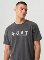 A man wearing a dark gray washed t-shirt with 'G.O.A.T GOD OVER ALL THINGS' print across the chest.