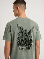 Sage green T-shirt with a winged warrior defeating a dragon and the text “VICTORY OVER DARKNESS” and “REVELATION 12.”