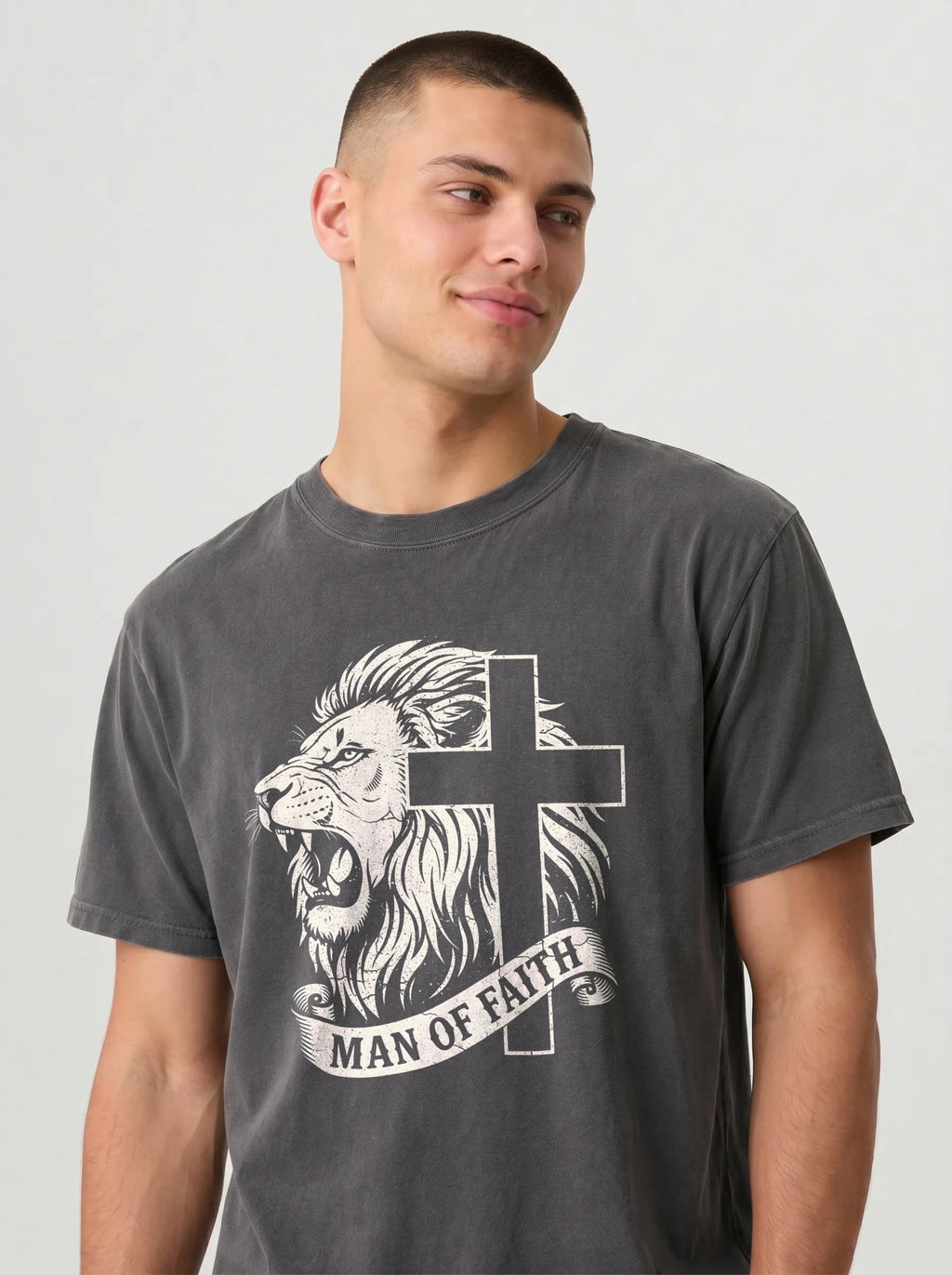 A man wearing a dark gray graphic t-shirt featuring a white illustration of a lion and cross with the text 'MAN OF FAITH' on a light gray background.