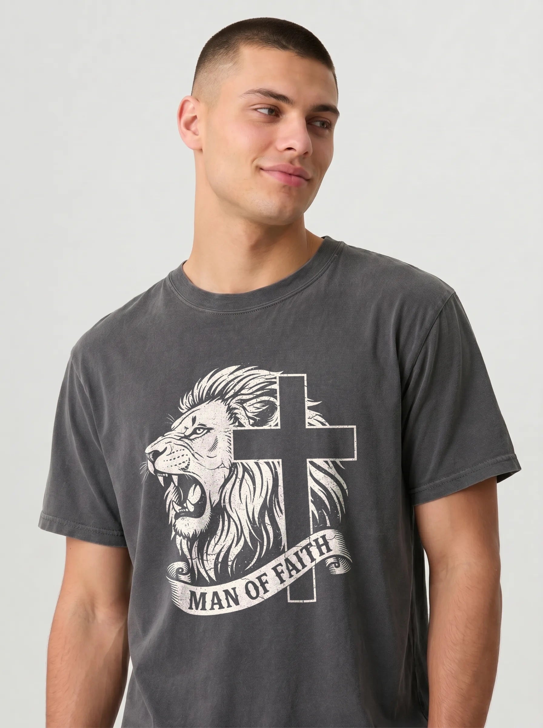 A man wearing a dark gray graphic t-shirt featuring a white illustration of a lion and cross with the text 'MAN OF FAITH' on a light gray background.