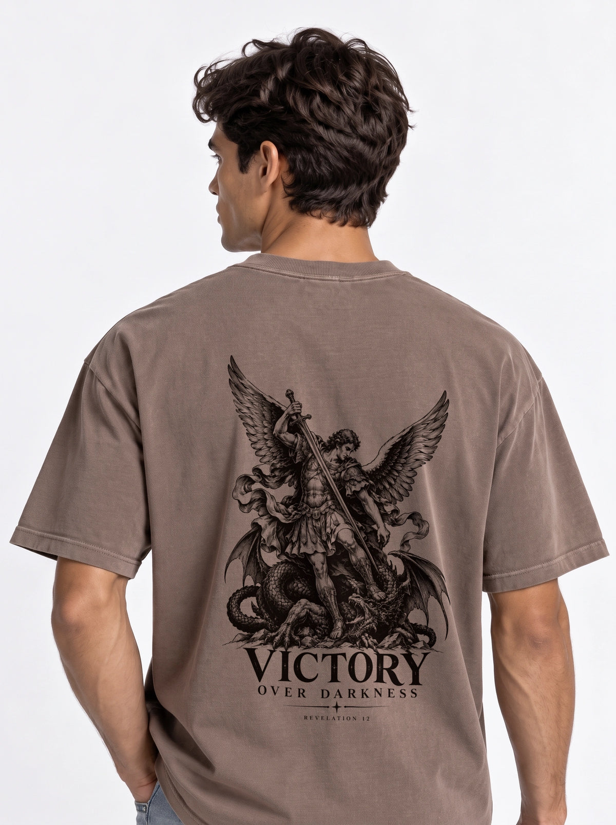 Brown T-shirt with a winged warrior defeating a dragon and the text “VICTORY OVER DARKNESS” and “REVELATION 12.”