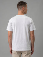 A man viewed from the back wearing a plain white short-sleeve crewneck t-shirt and beige pants, set against a solid gray studio background.