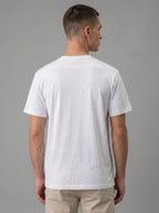 A man viewed from the back wearing a plain white short-sleeve crewneck t-shirt and beige pants, set against a solid gray studio background.