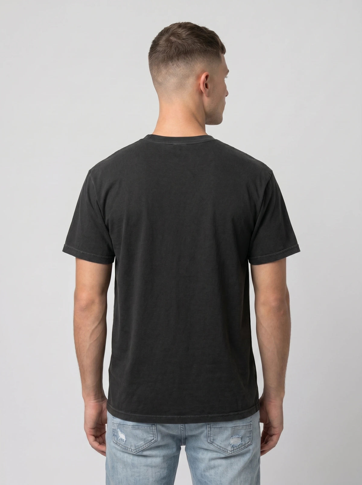 A man viewed from behind wearing a plain black short-sleeve t-shirt and light blue jeans, standing against a neutral light gray background.