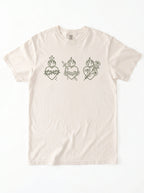 An off-white short-sleeve t-shirt with three dark green Sacred Heart line-art graphics across the chest, displayed flat against a white background.