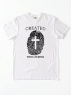 A white short-sleeve crewneck t-shirt with a black graphic print on the front. The graphic features the text 'CREATED WITH A PURPOSE' surrounding a fingerprint design where the center of the fingerprint is shaped like a Christian cross.