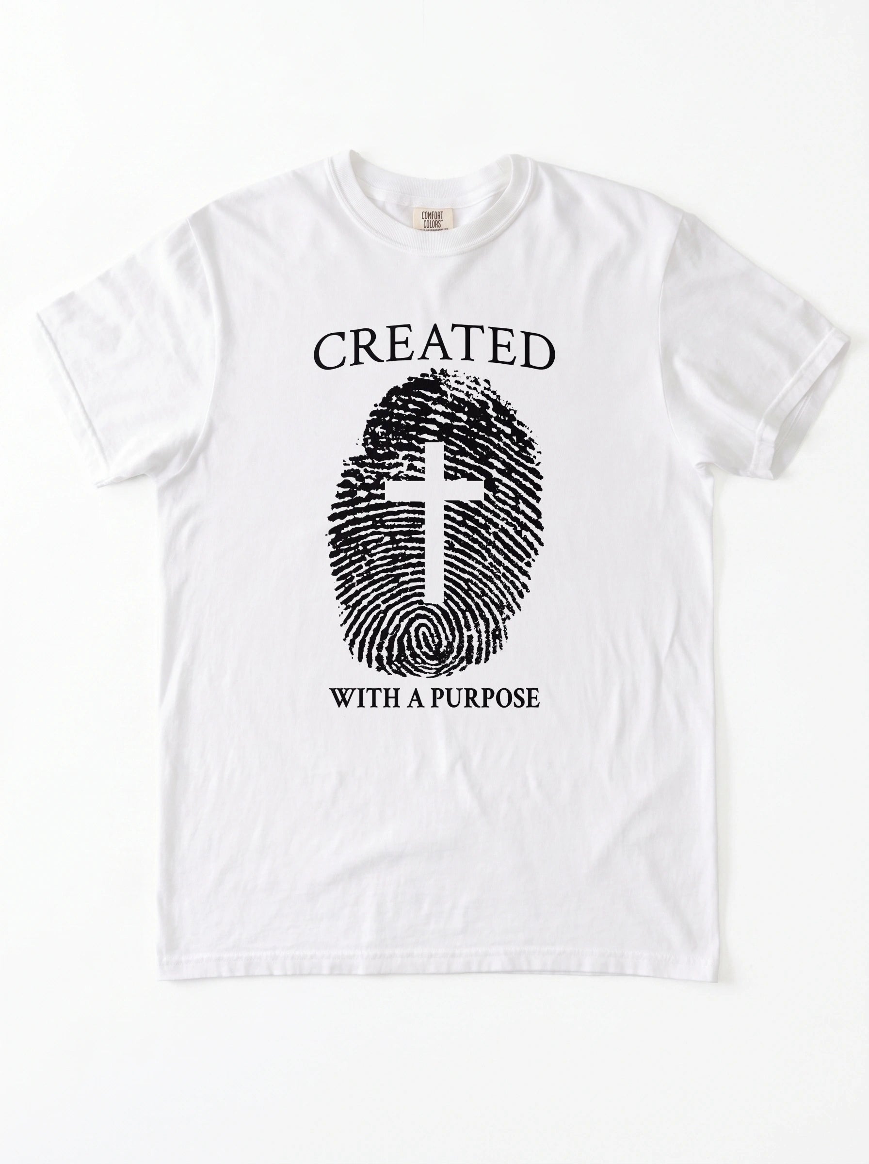 A white short-sleeve crewneck t-shirt with a black graphic print on the front. The graphic features the text 'CREATED WITH A PURPOSE' surrounding a fingerprint design where the center of the fingerprint is shaped like a Christian cross.