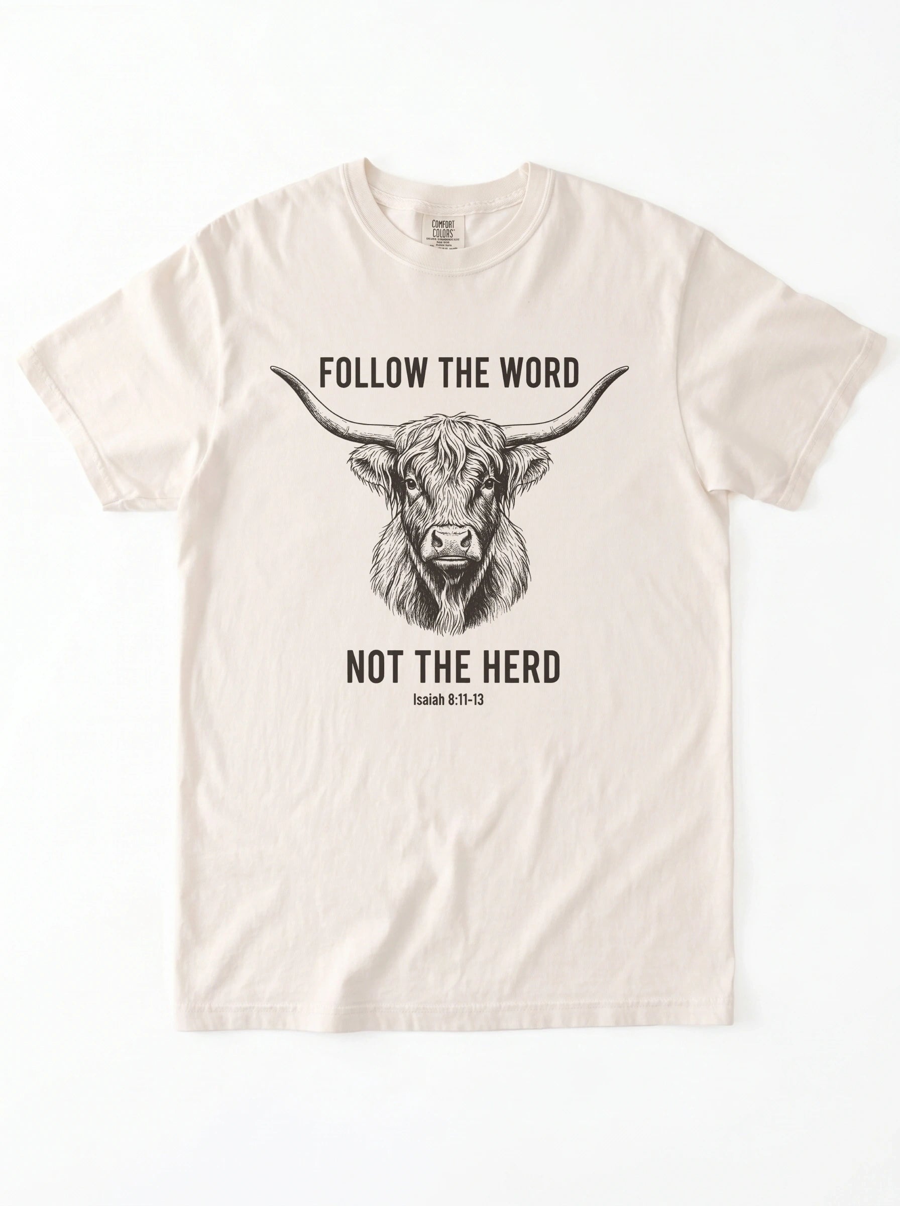An off-white short-sleeve crewneck t-shirt featuring a black graphic of a highland cow and the text 'FOLLOW THE WORD NOT THE HERD' and 'Isaiah 8:11-13'.