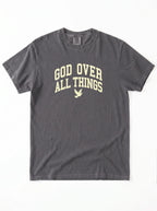A dark gray crewneck t-shirt with 'GOD OVER ALL THINGS' printed in a light beige collegiate-style font on the chest, accompanied by a small dove graphic below.