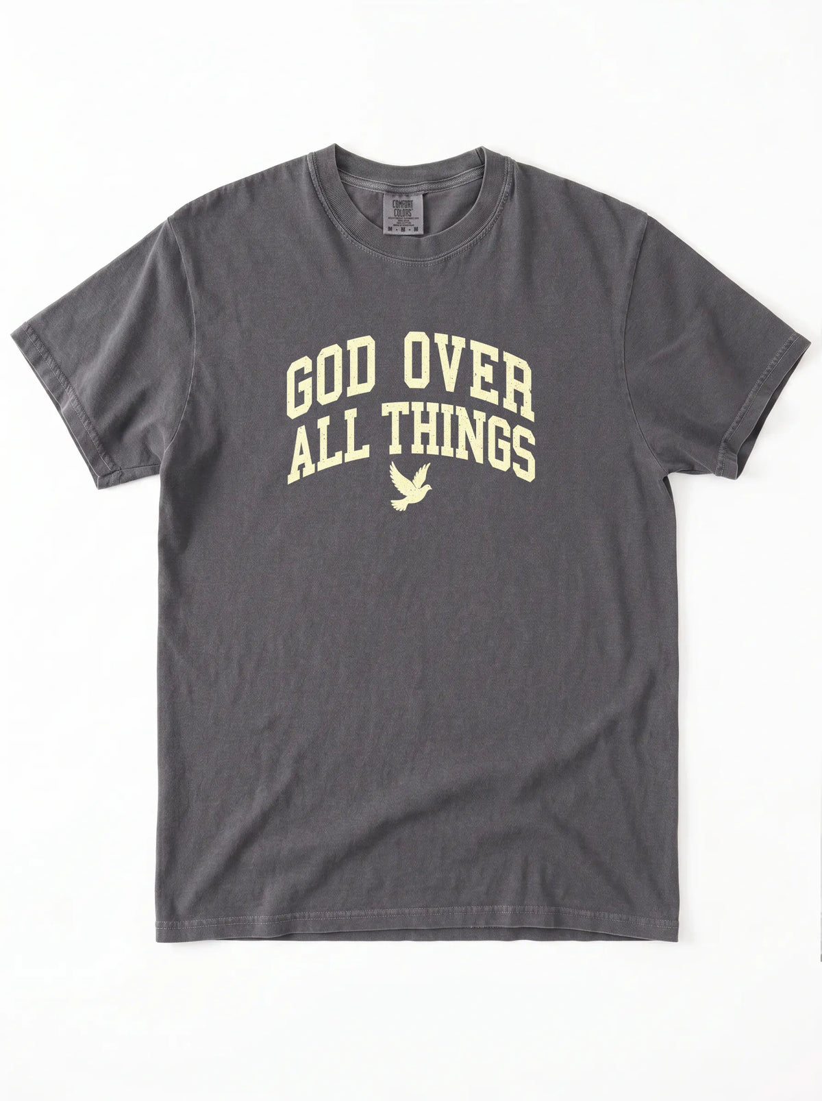 A dark gray crewneck t-shirt with 'GOD OVER ALL THINGS' printed in a light beige collegiate-style font on the chest, accompanied by a small dove graphic below.