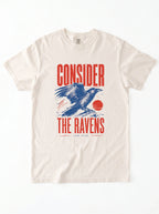 An off-white crewneck t-shirt featuring a graphic print of a blue raven and red text that reads 'CONSIDER THE RAVENS'.