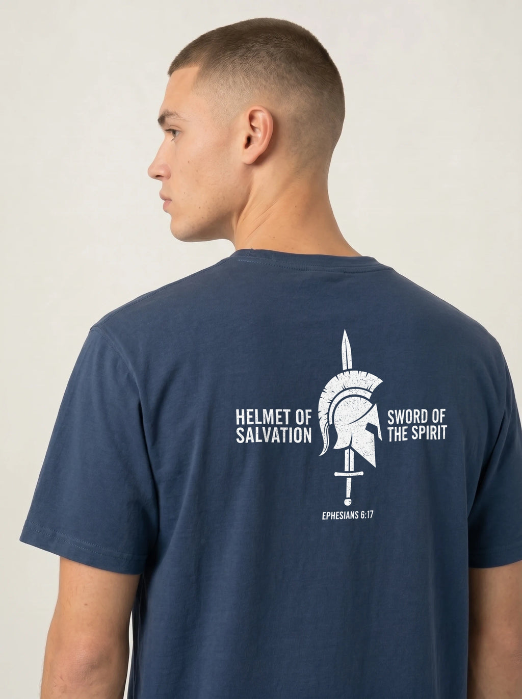 A man shown from the back wearing a navy blue t-shirt with a white graphic print on the back featuring a gladiator helmet and the text 'HELMET OF SALVATION' and 'SWORD OF THE SPIRIT'.