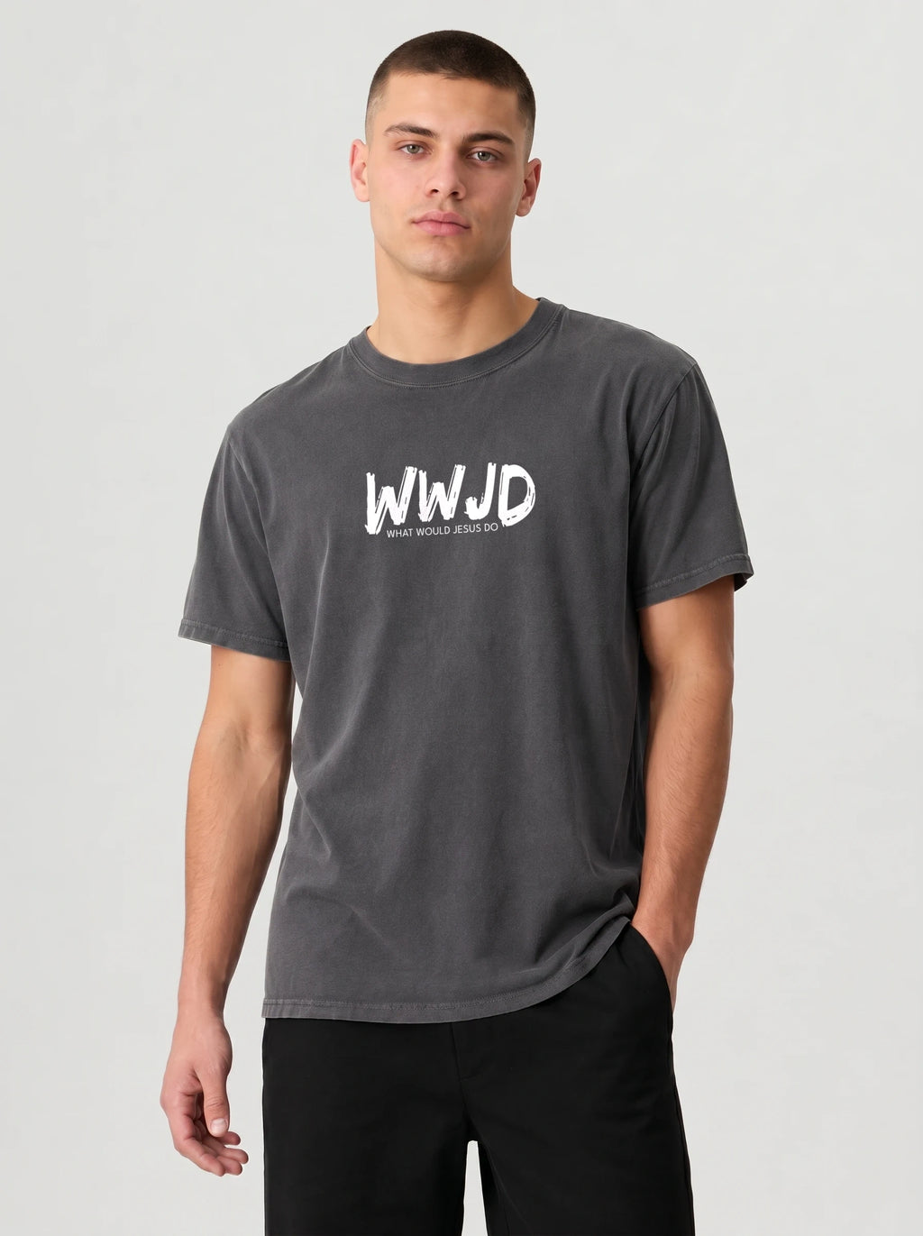 A man wearing a dark gray crewneck t-shirt with a white 'WWJD' graphic on the chest, paired with black pants, against a light gray studio background.