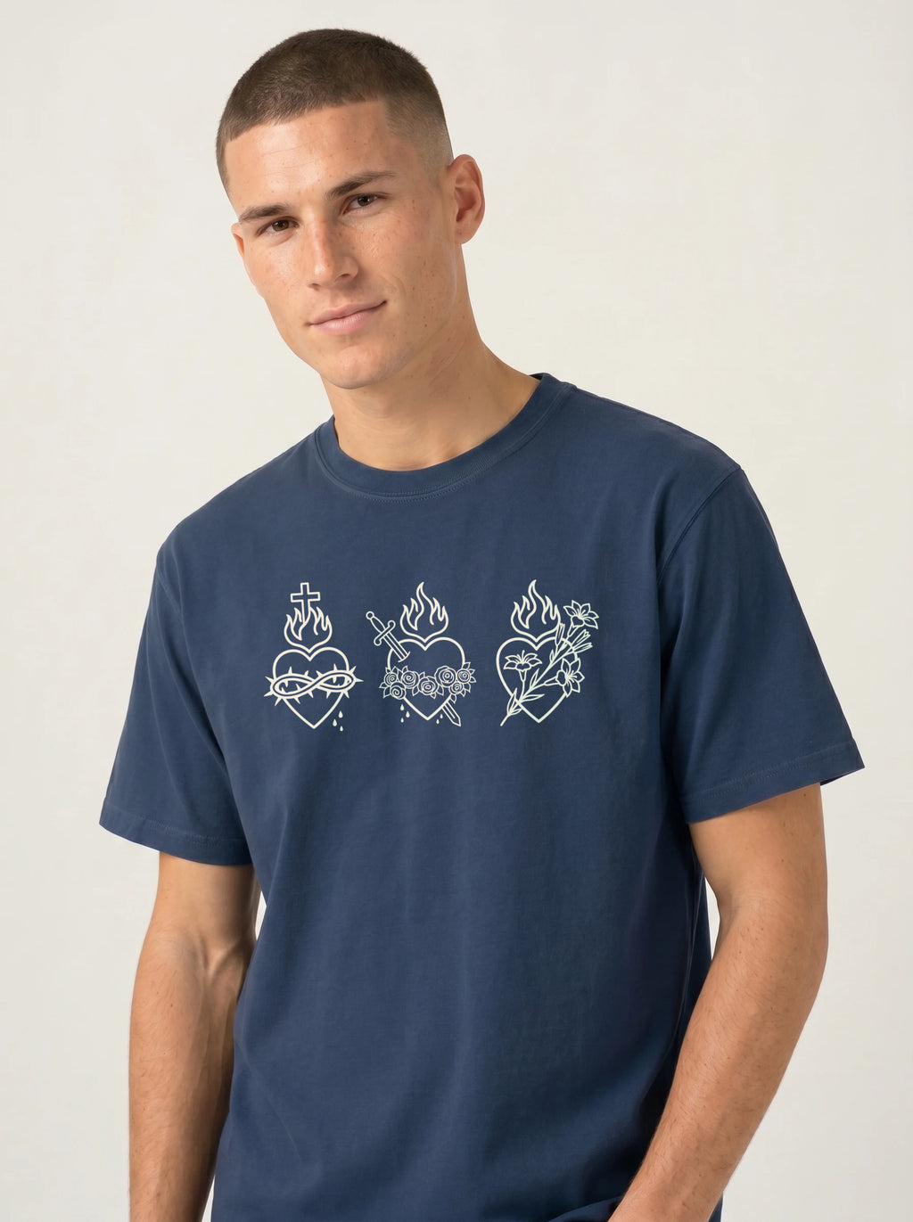 A man wearing a navy blue crewneck t-shirt with white line-art illustrations of Sacred Heart of Jesus on the chest, set against a plain light gray background.