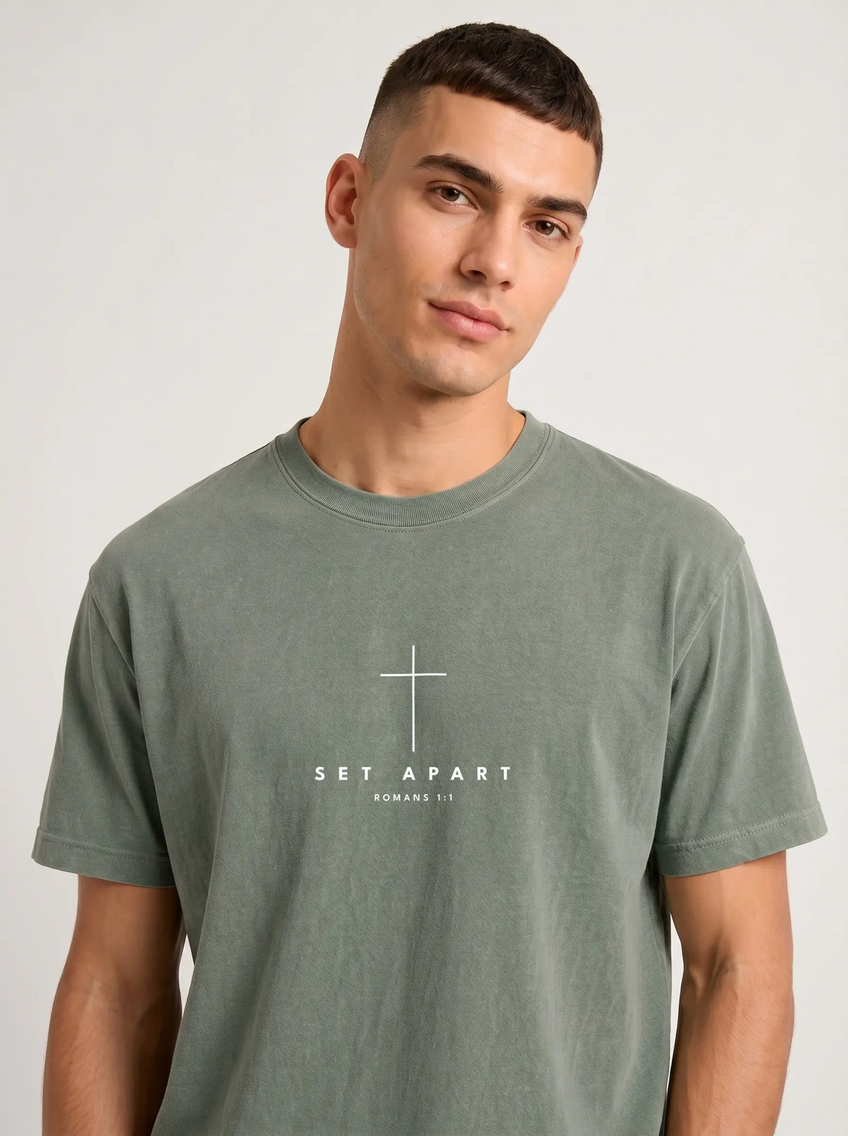 Person wearing a muted green T-shirt with a white cross above the text “Set Apart” and “Romans 1:1.”