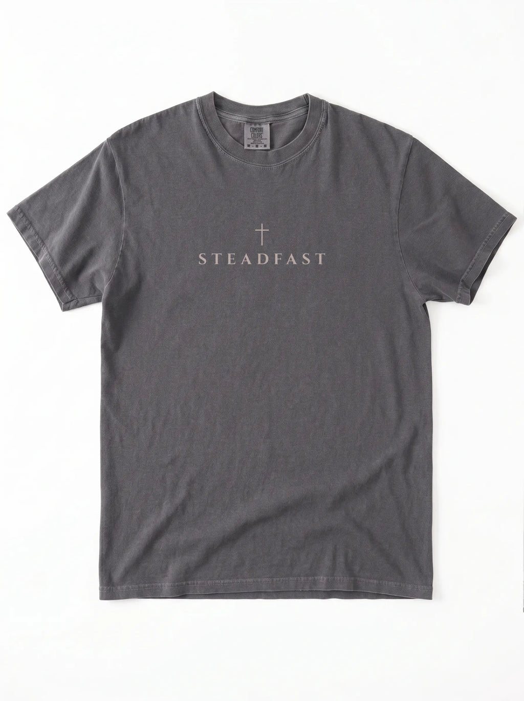 Faded charcoal T-shirt laid flat with a small cross above the word “Steadfast.”