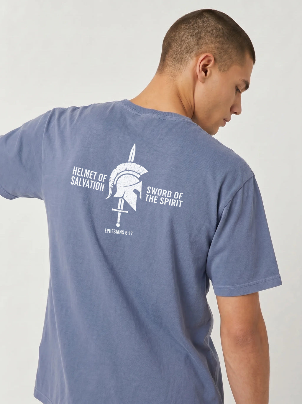 A man wearing a heathered slate blue t-shirt, viewed from the back. The shirt features a white graphic print of a Spartan helmet and sword with the text 'HELMET OF SALVATION' and 'SWORD OF THE SPIRIT' on the back.