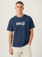 A man wearing a navy blue crewneck t-shirt with a white 'WWJD' graphic on the chest, paired with light beige pants, standing against a light gray studio background.