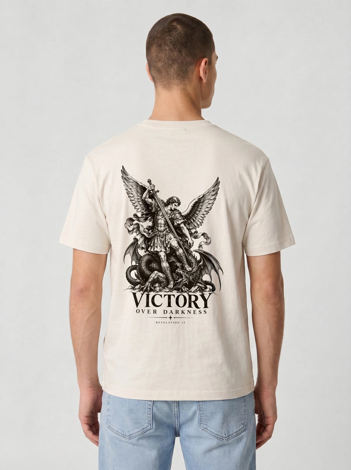 Cream T-shirt with a winged warrior defeating a dragon and the text “VICTORY OVER DARKNESS” and “REVELATION 12.”