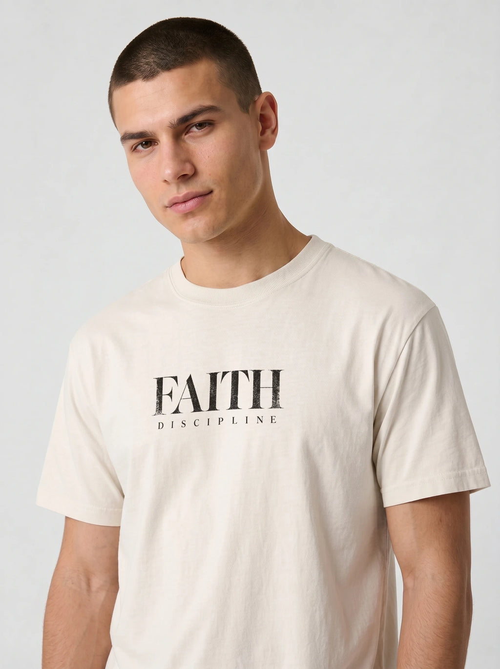 Person wearing a cream T-shirt with distressed black text reading “FAITH” and “DISCIPLINE.”