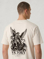 Cream T-shirt with a large winged warrior and dragon illustration above “VICTORY OVER DARKNESS” and “REVELATION 12.”