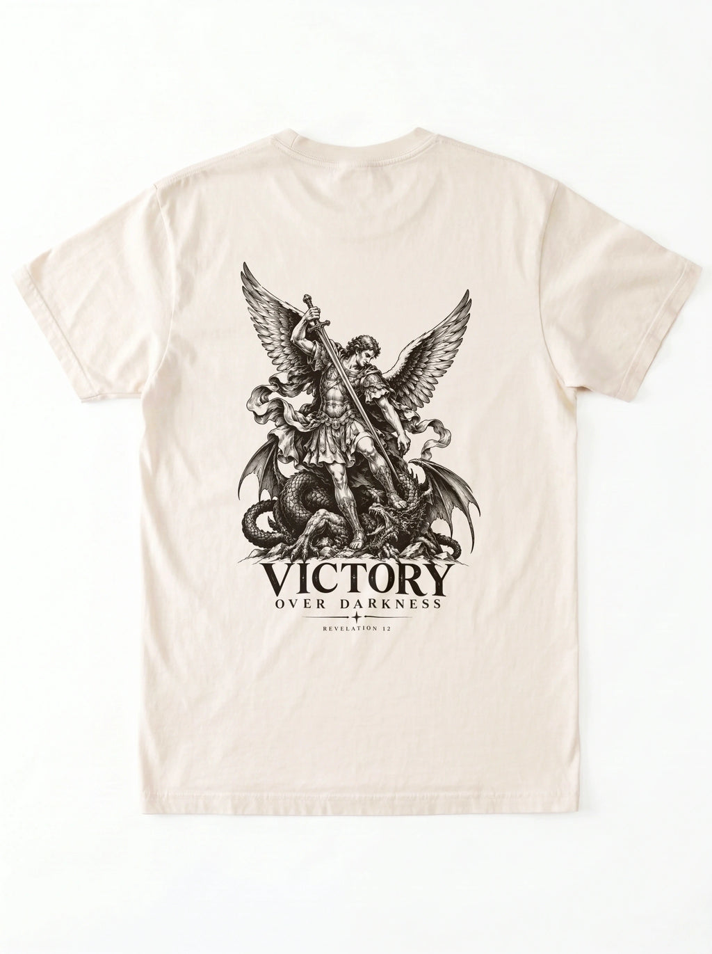 Cream T-shirt laid flat with a winged warrior defeating a dragon and the text “VICTORY OVER DARKNESS” and “REVELATION 12.”