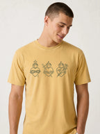 A man wearing a mustard yellow t-shirt with three Sacred Heart of Jesus line art graphics printed on the chest, set against a plain light gray background.