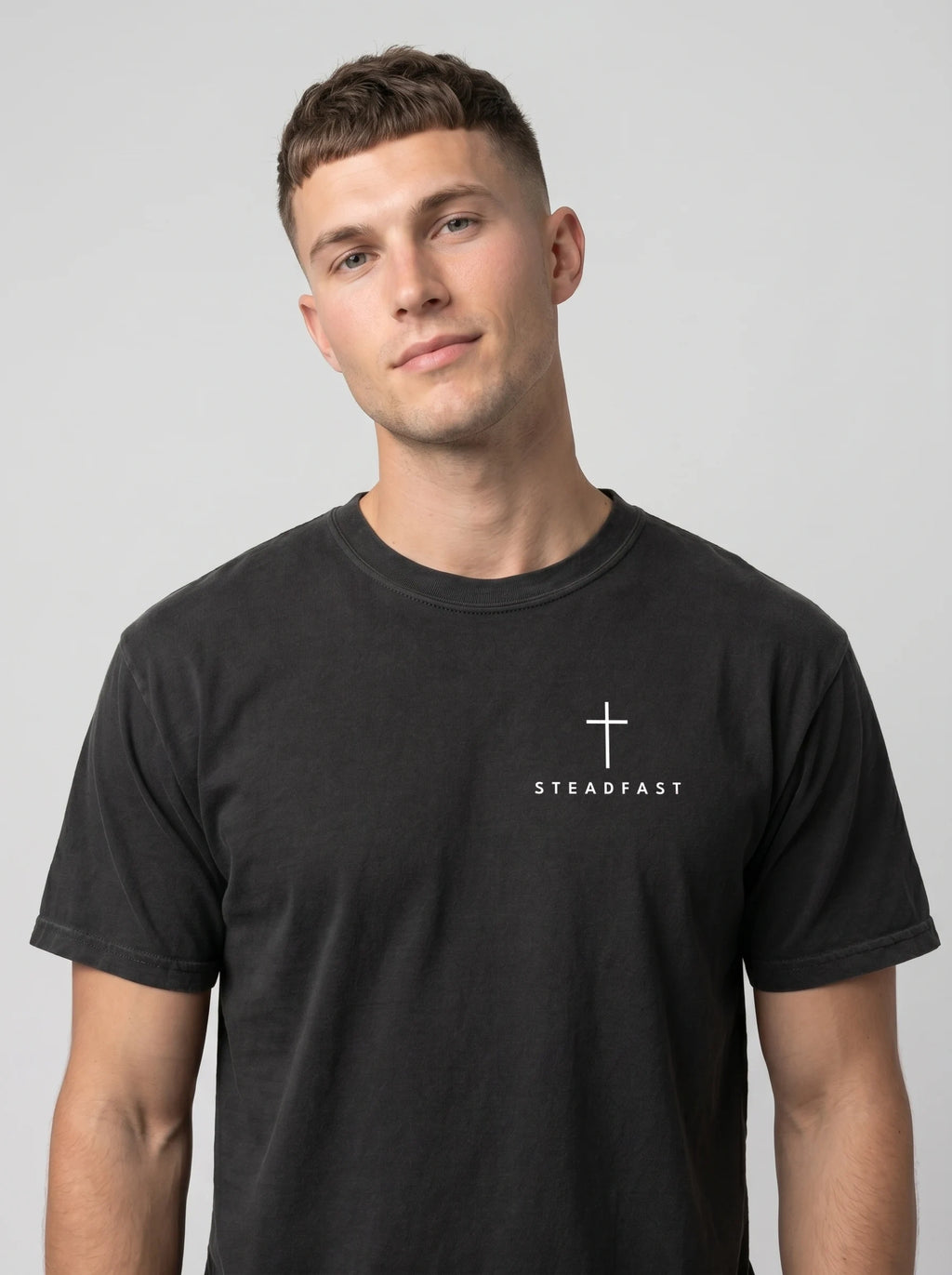 Person wearing a faded black T-shirt with a white cross and “STEADFAST” printed on the chest.