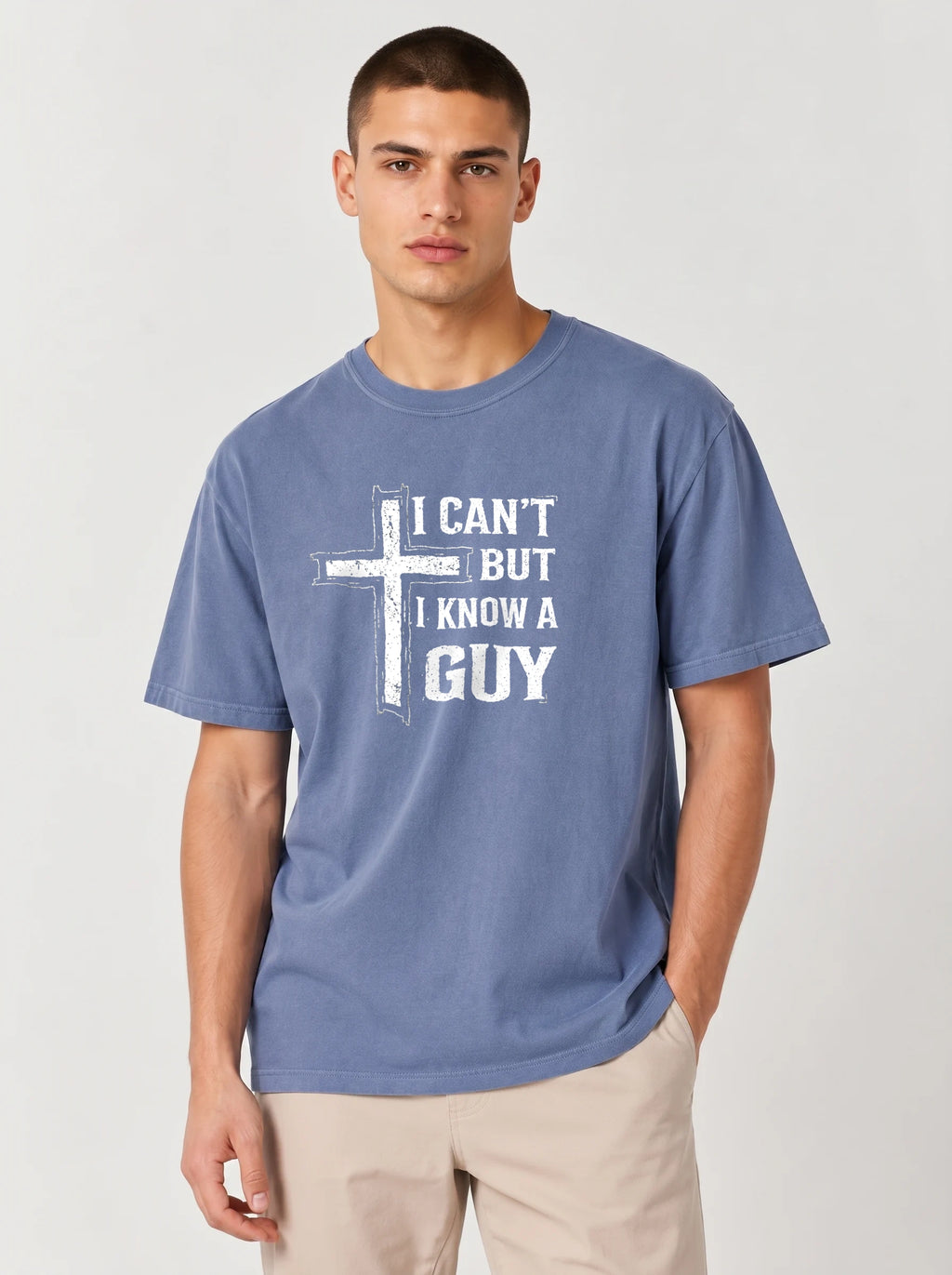 A man wearing a heathered blue crewneck t-shirt with a white graphic print of a cross and the text 'I CAN'T BUT I KNOW A GUY'.