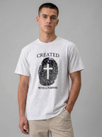 A man wearing a white crewneck t-shirt with a black graphic print of a fingerprint cross and the text 'CREATED WITH A PURPOSE'.